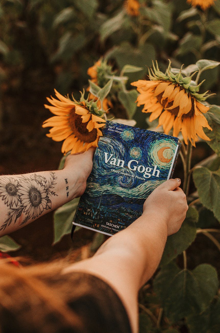 person holding van gogh book beside sunflowers